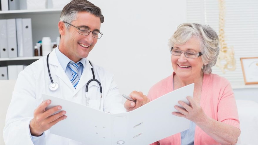 Arzt und Patientn die gemeinsam lachend in einen Ordner schauen