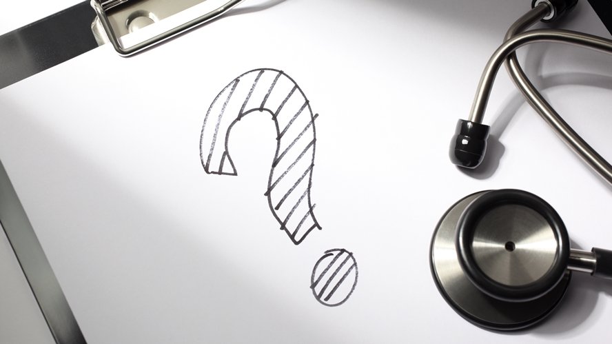 Schwarzes Fragezeichen gezeichnet auf einem Papier und ein darauf liegendes Stetoskop