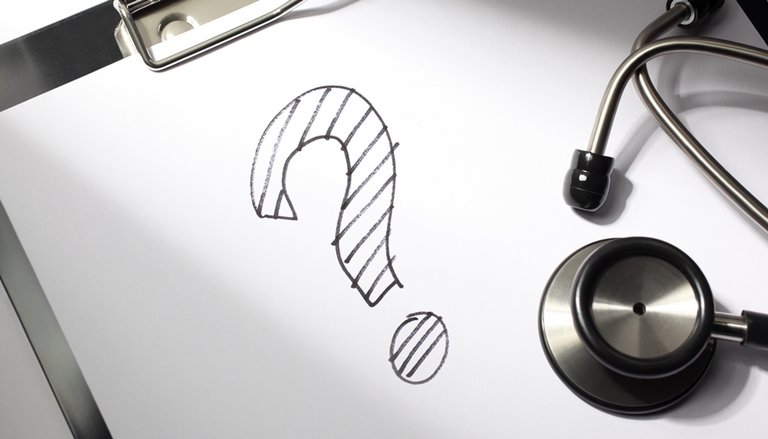 Schwarzes Fragezeichen gezeichnet auf einem Papier und ein darauf liegendes Stetoskop