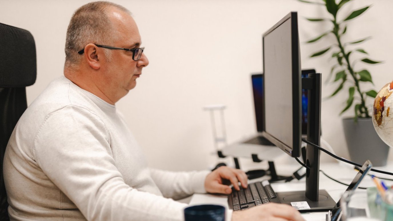 Mann sitzt an einem Schreibtisch vor einem Computer