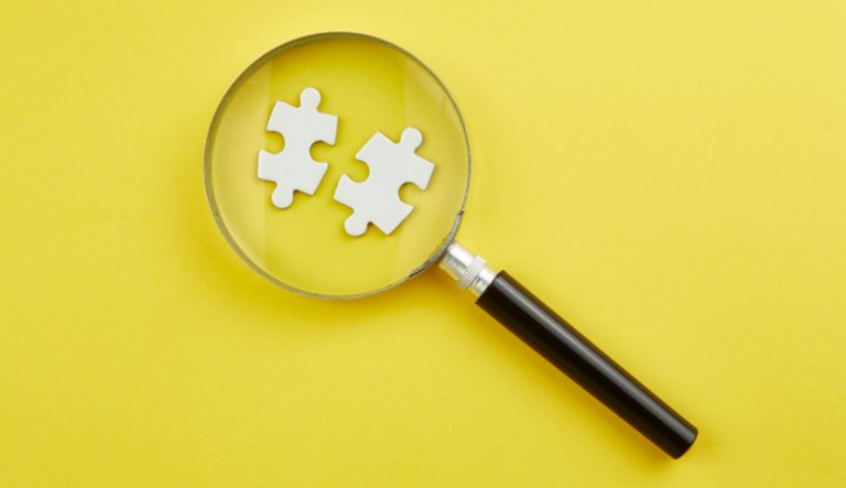 Lupe vergrößert zwei Puzzleteile vor gelbem Hintergrund 